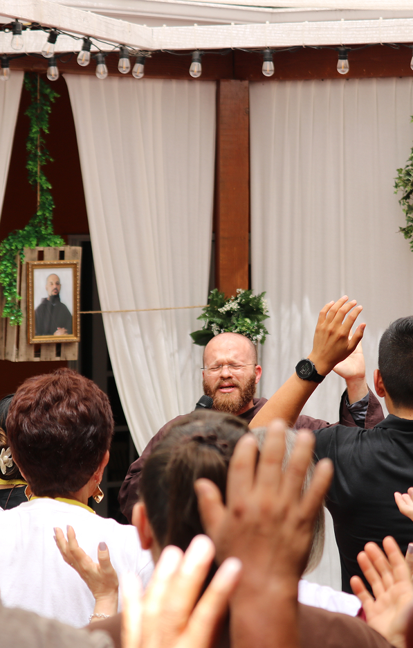 Friar speaking to a group of people with raised hands